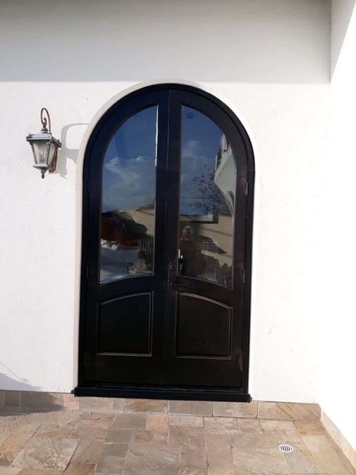 Arched black front door with glass panels on a white stucco wall and stone patio