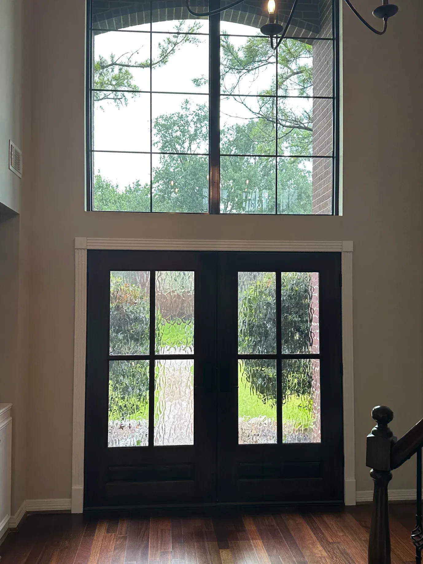 Black double front doors with glass panes beneath a large arched window in a foyer