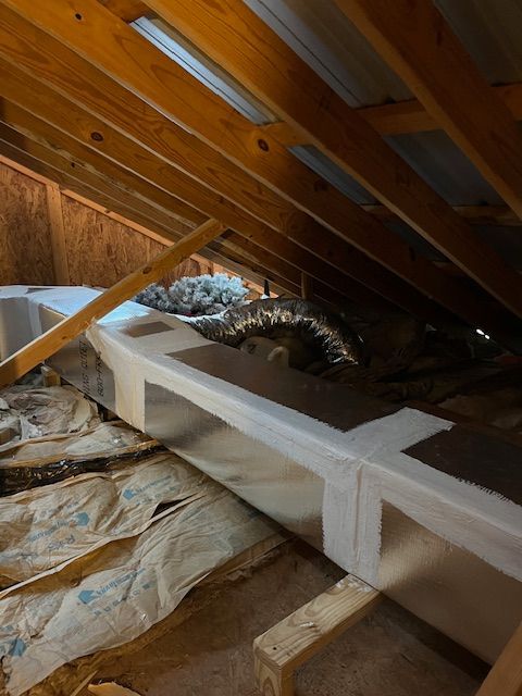 Attic with exposed wooden rafters, insulation, and a white duct wrapped in tape