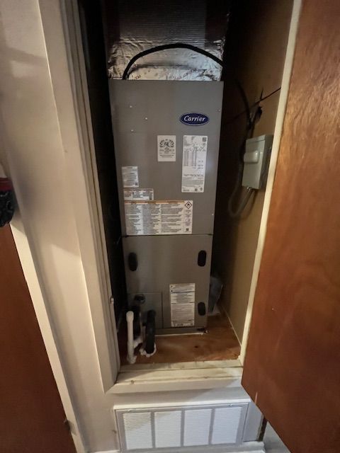 Open HVAC unit in a narrow closet with exposed pipes and wiring