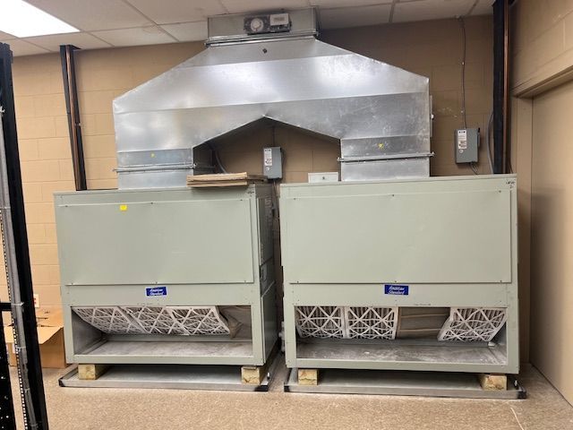 Two large beige HVAC units with metal ductwork in a utility room