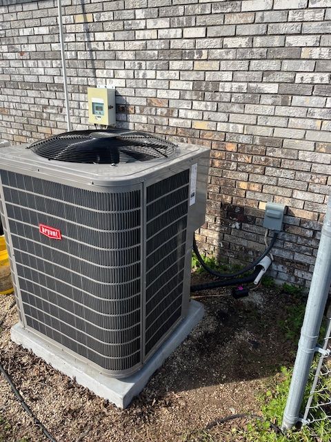 Outdoor air conditioner unit beside a brick wall with exposed pipes and wiring