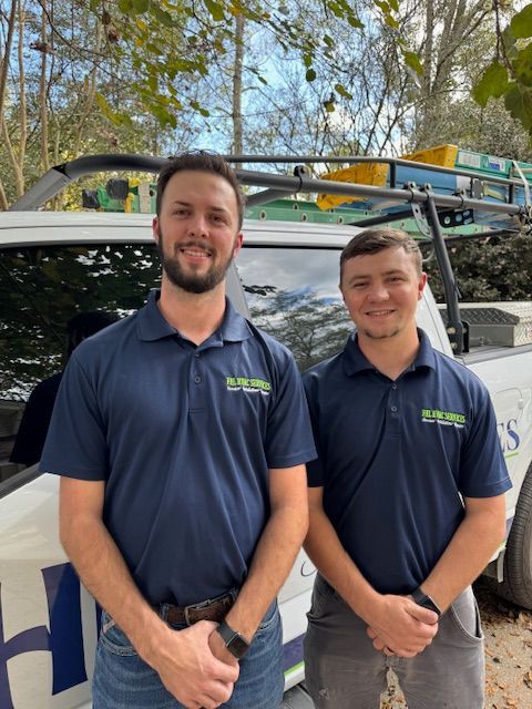 Two smiling team members in navy polos stand beside a service van outdoors.