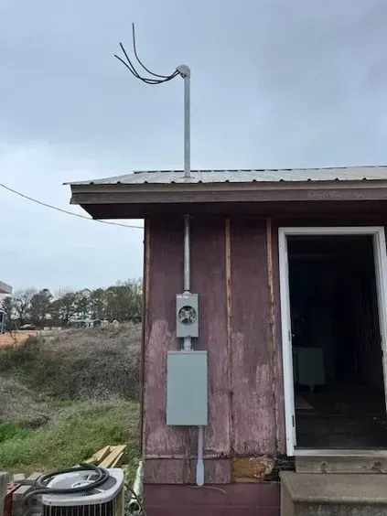 Utility meter box and conduit on the side of a small weathered building with an open doorway.