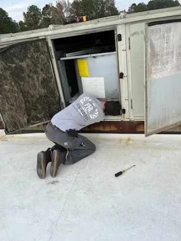 Person kneeling beside an open outdoor utility cabinet, inspecting equipment in the snow