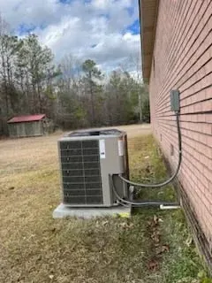 Outdoor air conditioning unit beside a brick house on a grassy yard under a cloudy sky