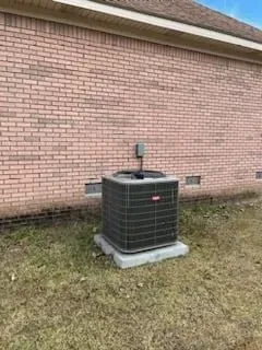 Outdoor air conditioner unit against a brick wall on grass