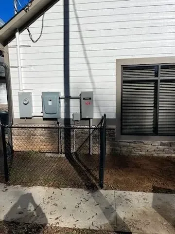 Backyard side of a white house with utility boxes, a chain-link fence gate, and a window