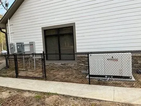 Backyard patio with chain-link fence and white house wall, featuring a generator unit near a sliding door