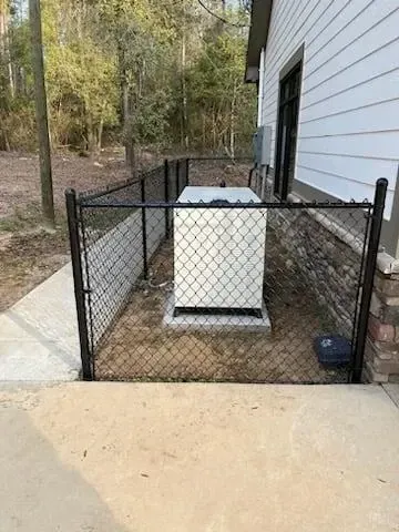 Chain-link fenced patio with a white outdoor unit beside a house wall