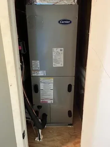 Carrier furnace unit in a narrow utility closet with exposed pipes and wiring.