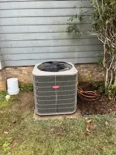 Outdoor air conditioner unit beside a house, with a hose and bucket nearby