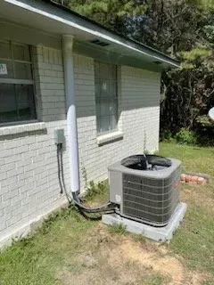 Outdoor air conditioning unit beside a white brick house with attached white conduit.