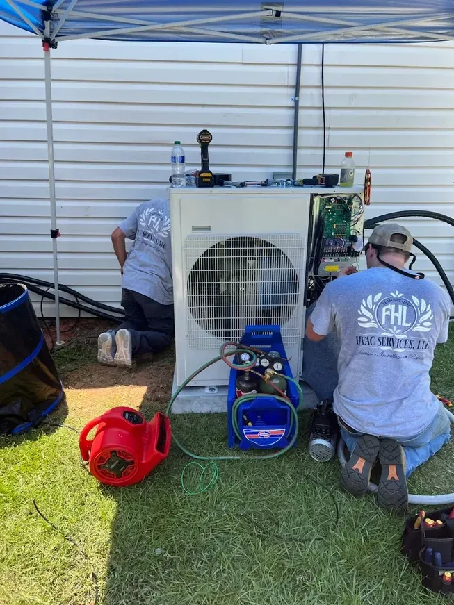 Technicians servicing a large outdoor HVAC unit under a canopy, with tools and hoses on grass.