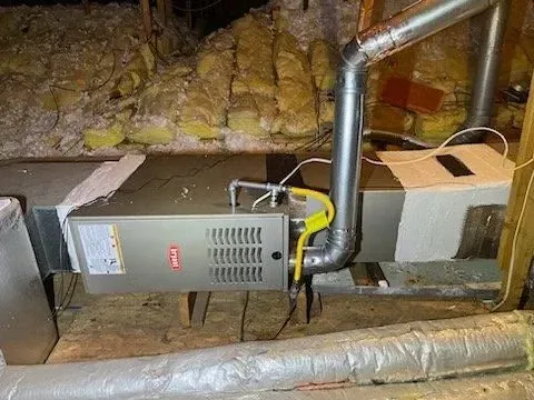 Gray furnace and ductwork in a crawlspace with exposed insulation and pipes