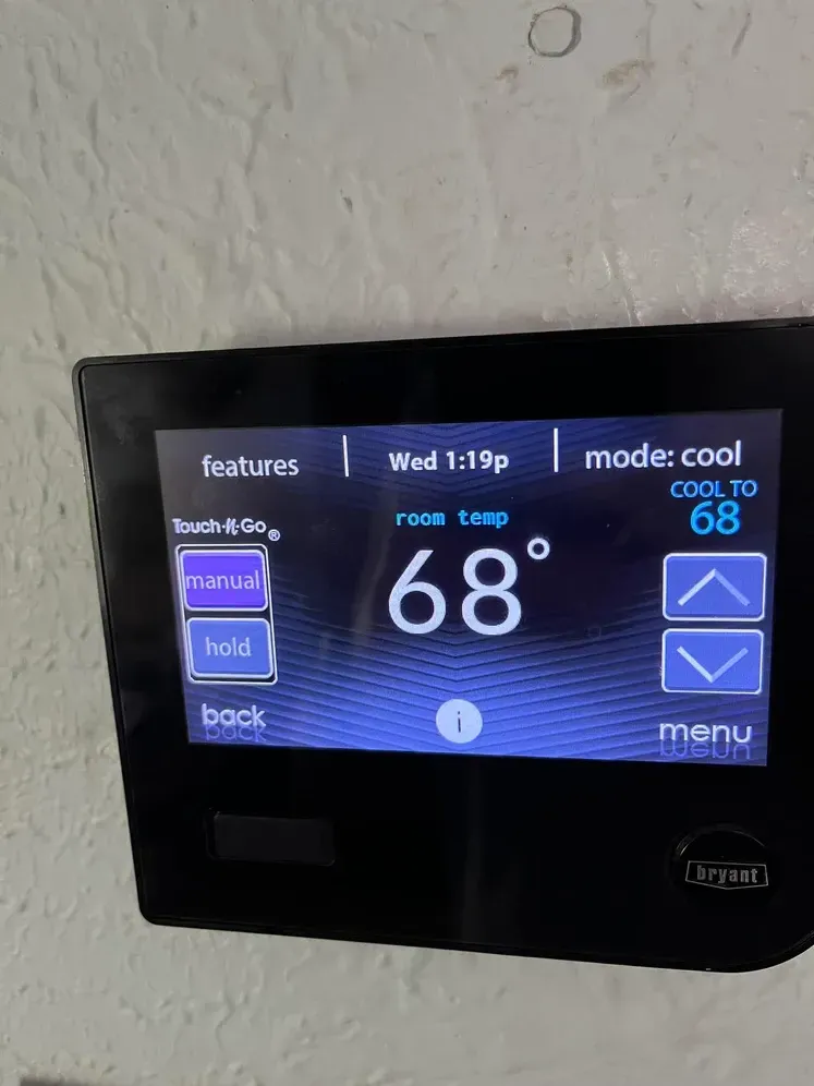 Black touchscreen thermostat on a wall, showing 68°F in cool mode with blue controls.