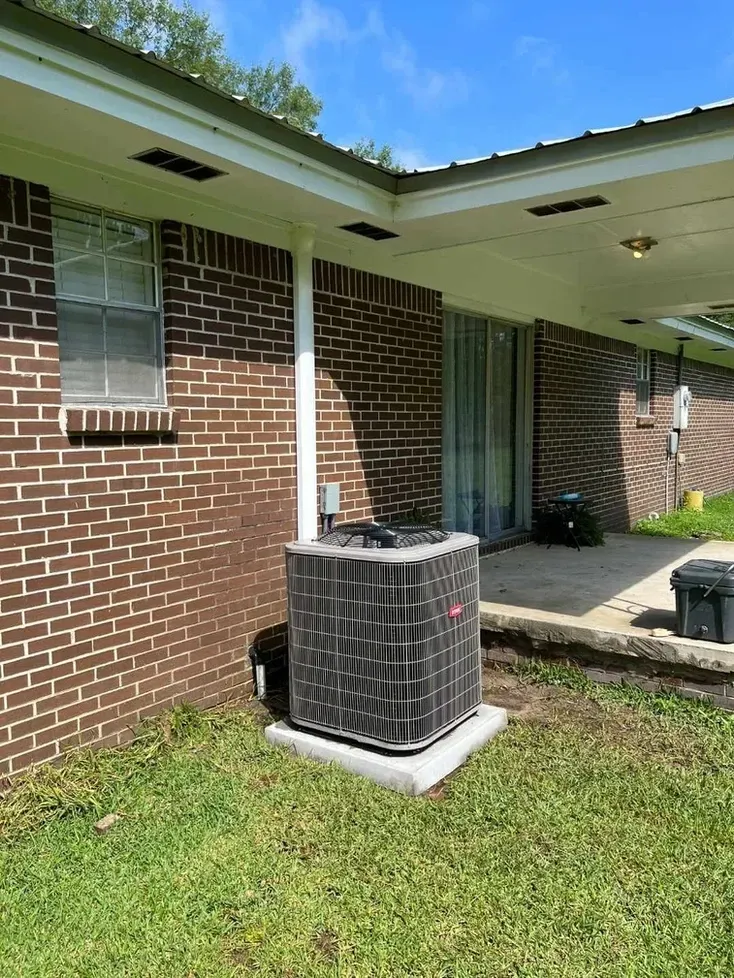 Brick house exterior with central air conditioner unit on a concrete pad under the roof overhang.