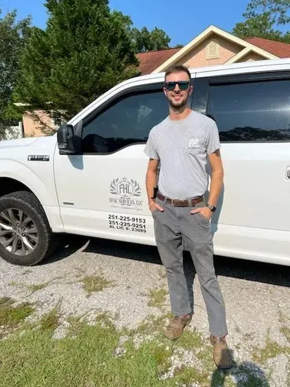 Man standing beside a white work truck in front of a house, wearing sunglasses and a gray T-shirt.