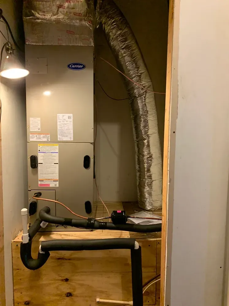 Utility closet with HVAC unit, exposed ductwork, and a metal pipe barrier in a narrow hallway.