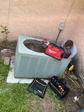 Technician working on a rooftop HVAC unit beside tools and a red tool bag.