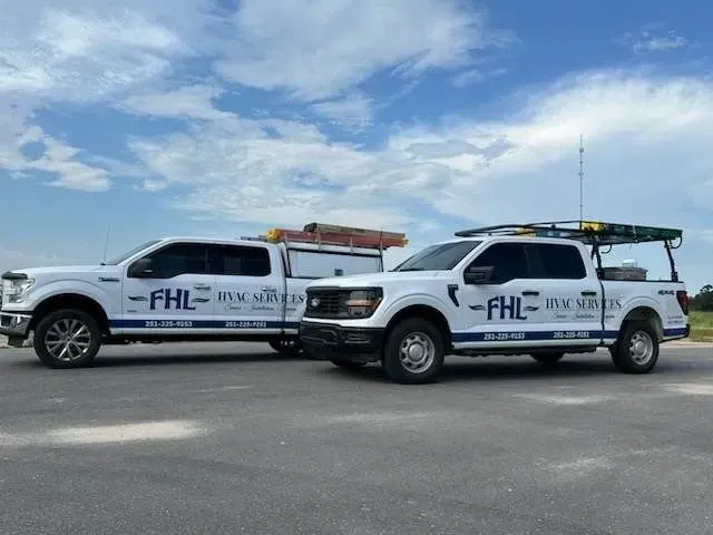 Two white FHIL utility trucks parked side by side on an open lot under a blue sky.