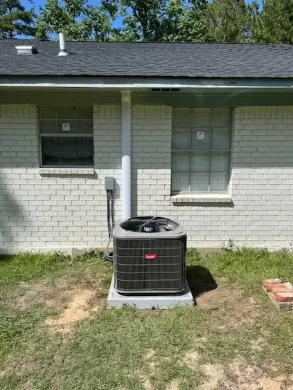Outdoor air conditioner unit beside a white brick house with two windows and a grassy yard