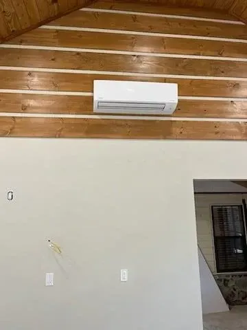 Interior wall with white split air conditioner beneath a wooden ceiling and a doorway on the right.
