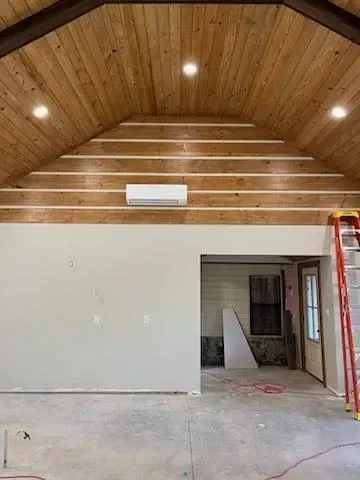 Empty room with wood-paneled vaulted ceiling, white walls, and unfinished floor under construction