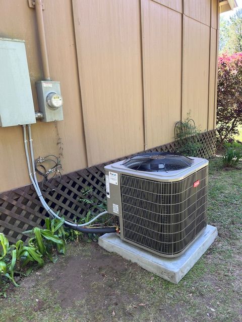 Outdoor air conditioning unit beside a beige house, with electrical meter and conduit on the wall