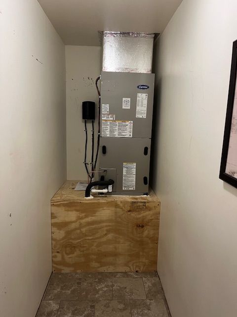 Narrow utility closet with a furnace, vent, wiring, and plywood-covered floor area.
