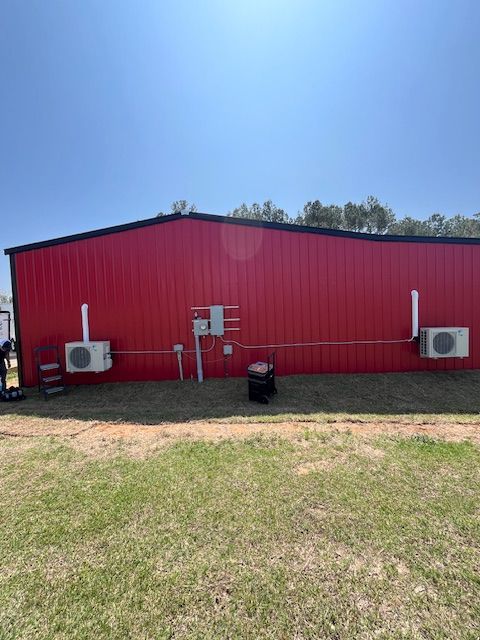 Red metal building exterior with three wall-mounted AC units under a clear blue sky.