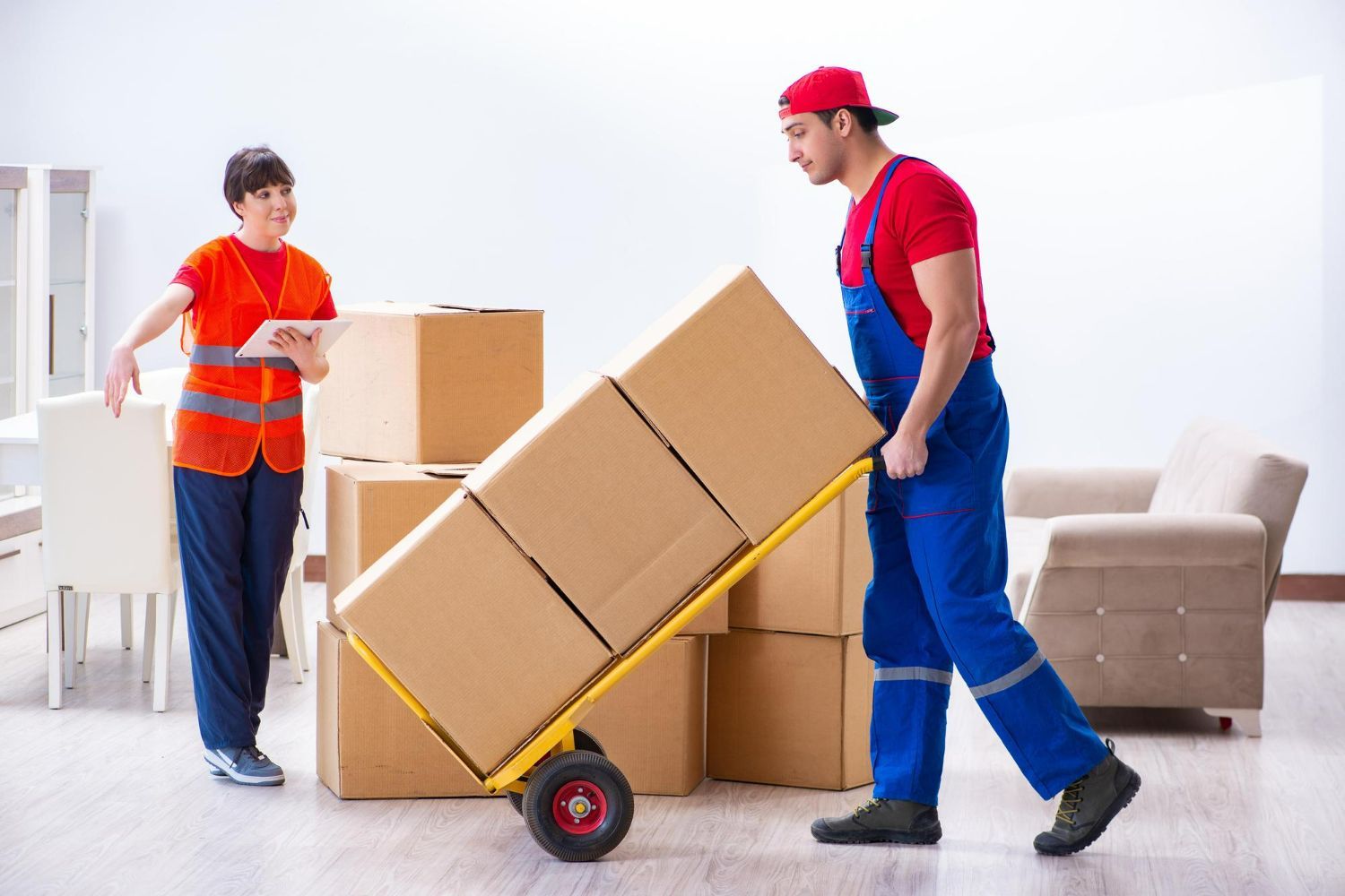 Two movers in orange and blue unload cardboard boxes in a bright living room.