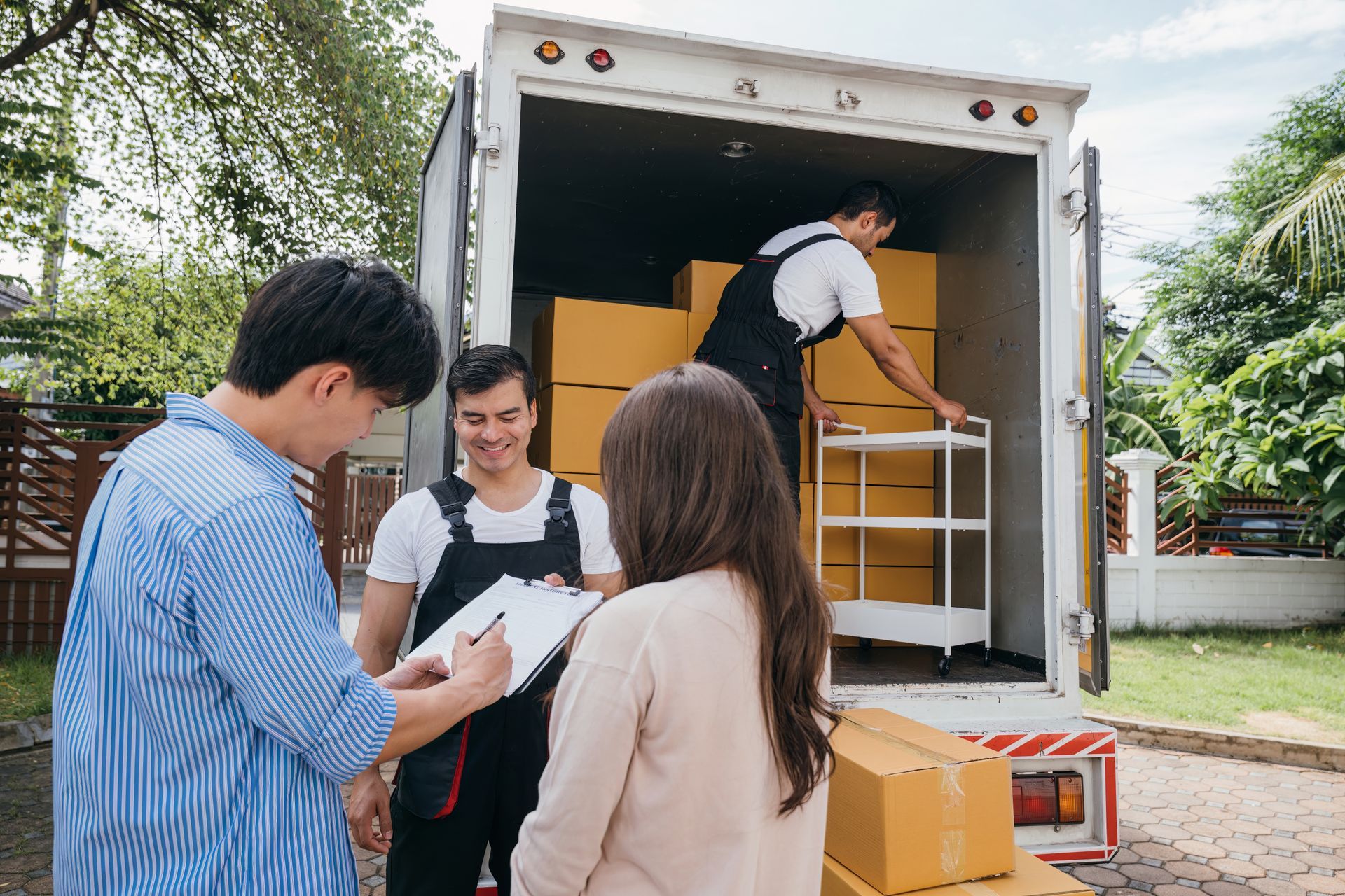 People signing paperwork with movers, unloading boxes from a moving truck outdoors.