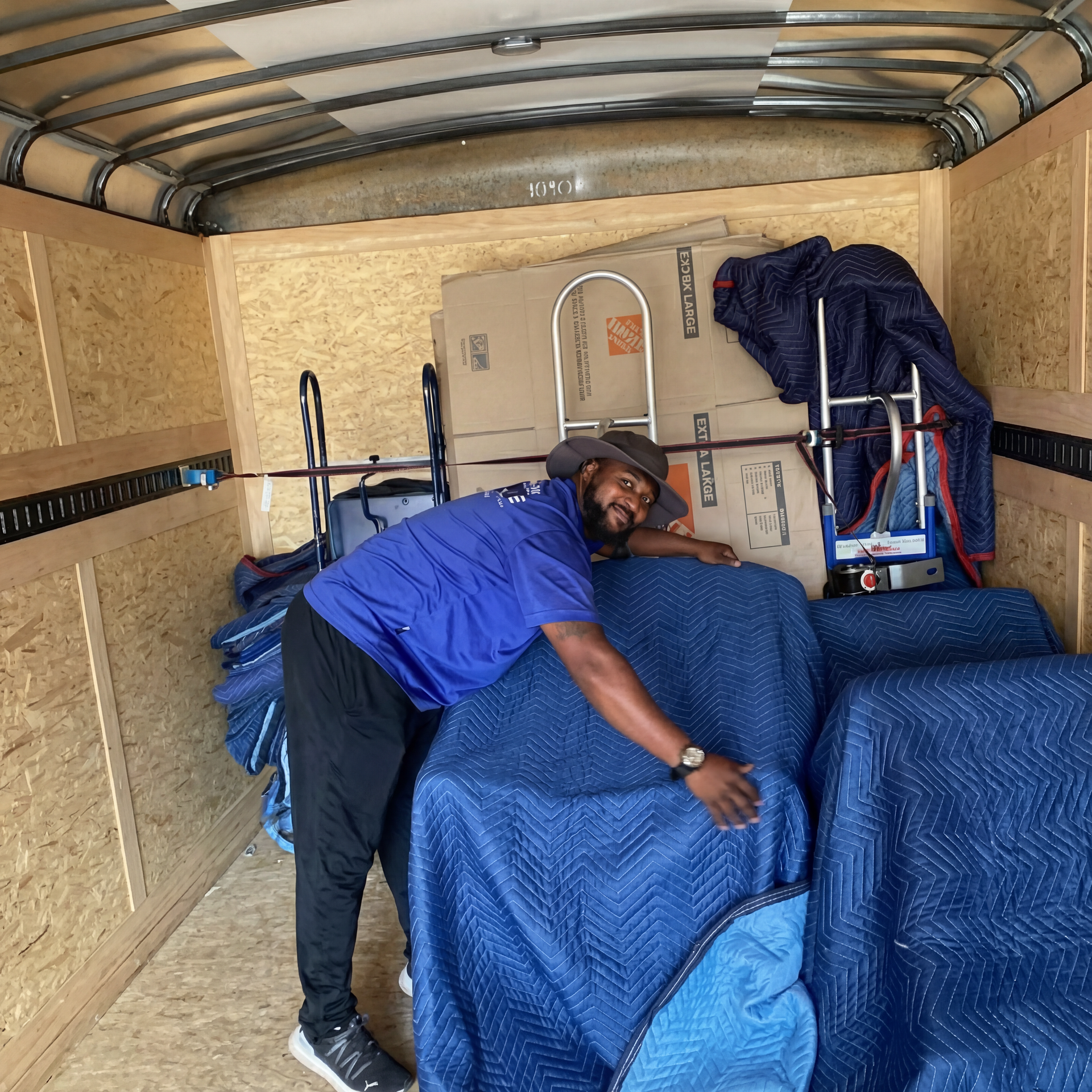 Person in a blue shirt loading a blue-covered couch into a trailer moving truck
