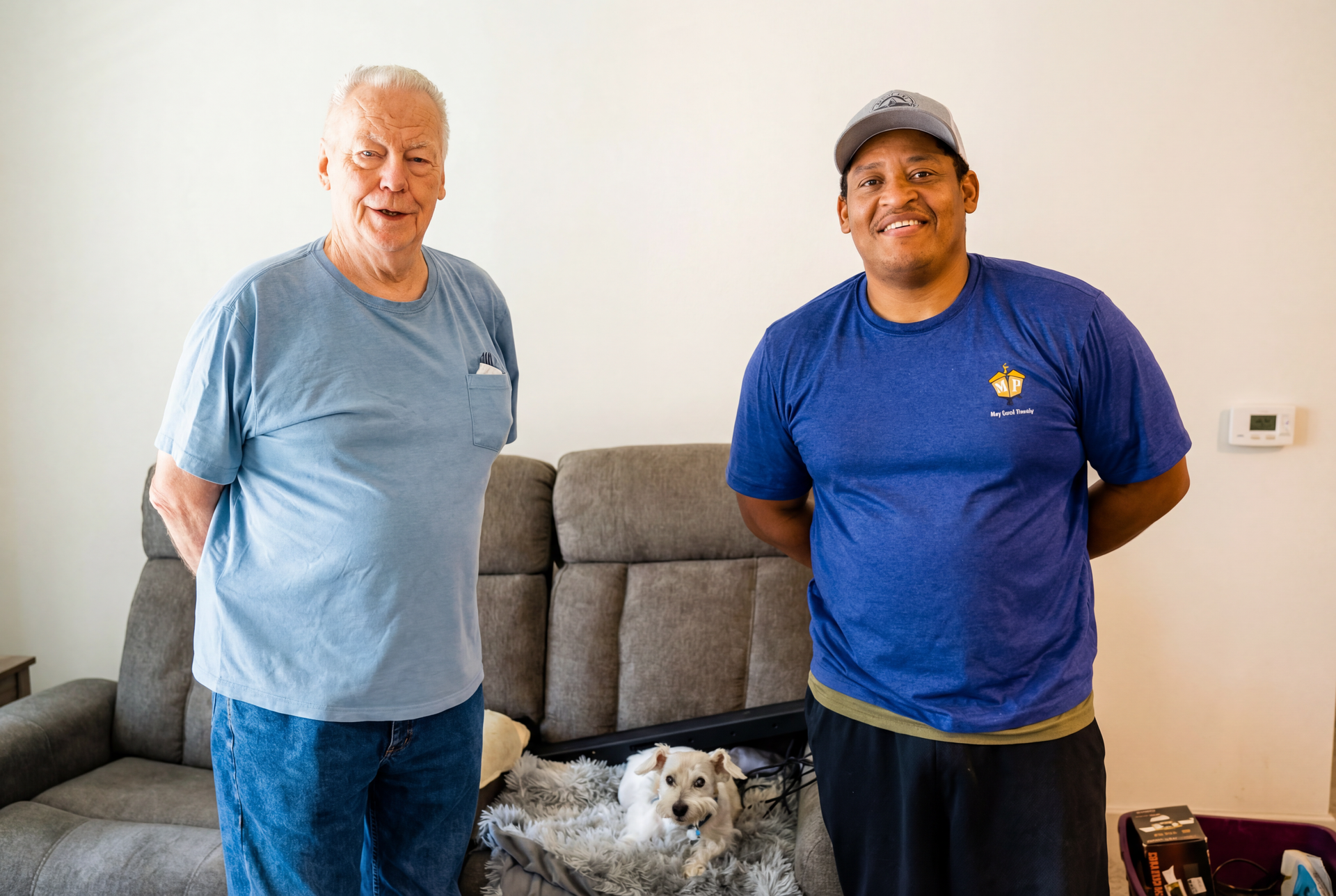 Two people standing in a living room with a dog on the couch between them