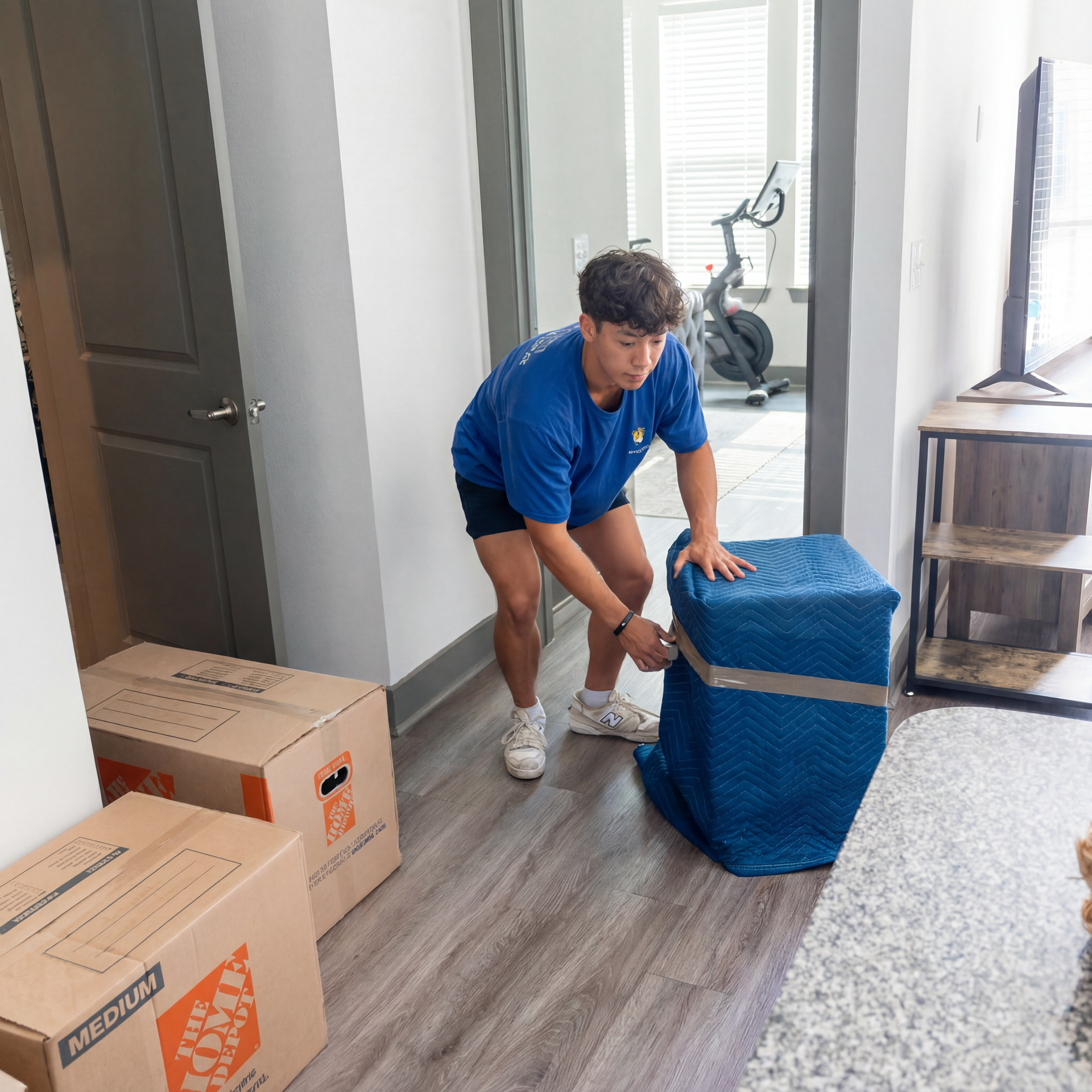 Mover in blue shirt lifting a blue-wrapped box beside packed moving boxes in a home hallway