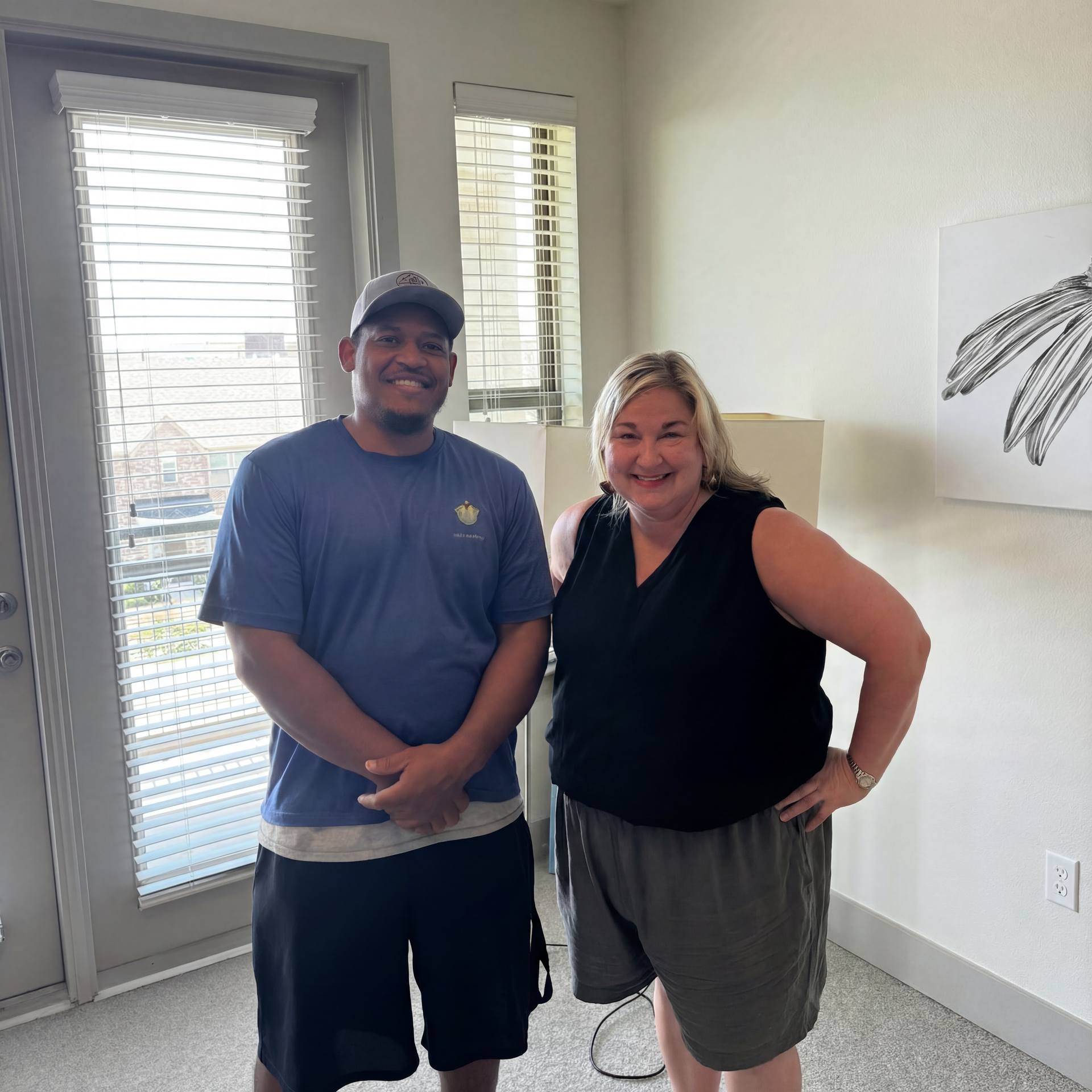 Two people smiling and posing together in a bright room by a window