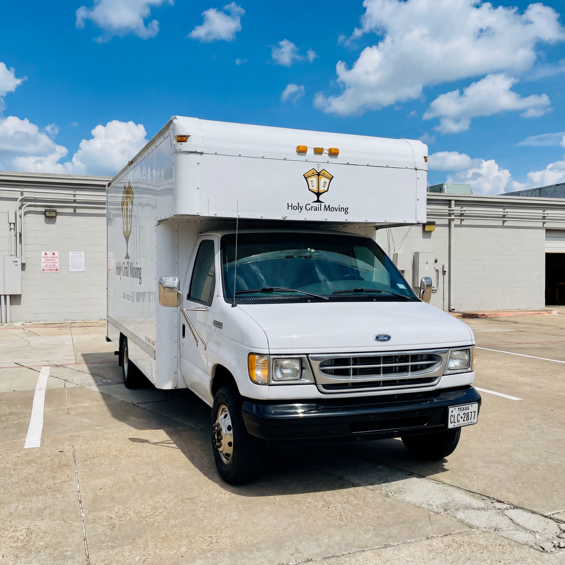 White delivery box truck parked in a lot under a blue sky, front facing the camera.