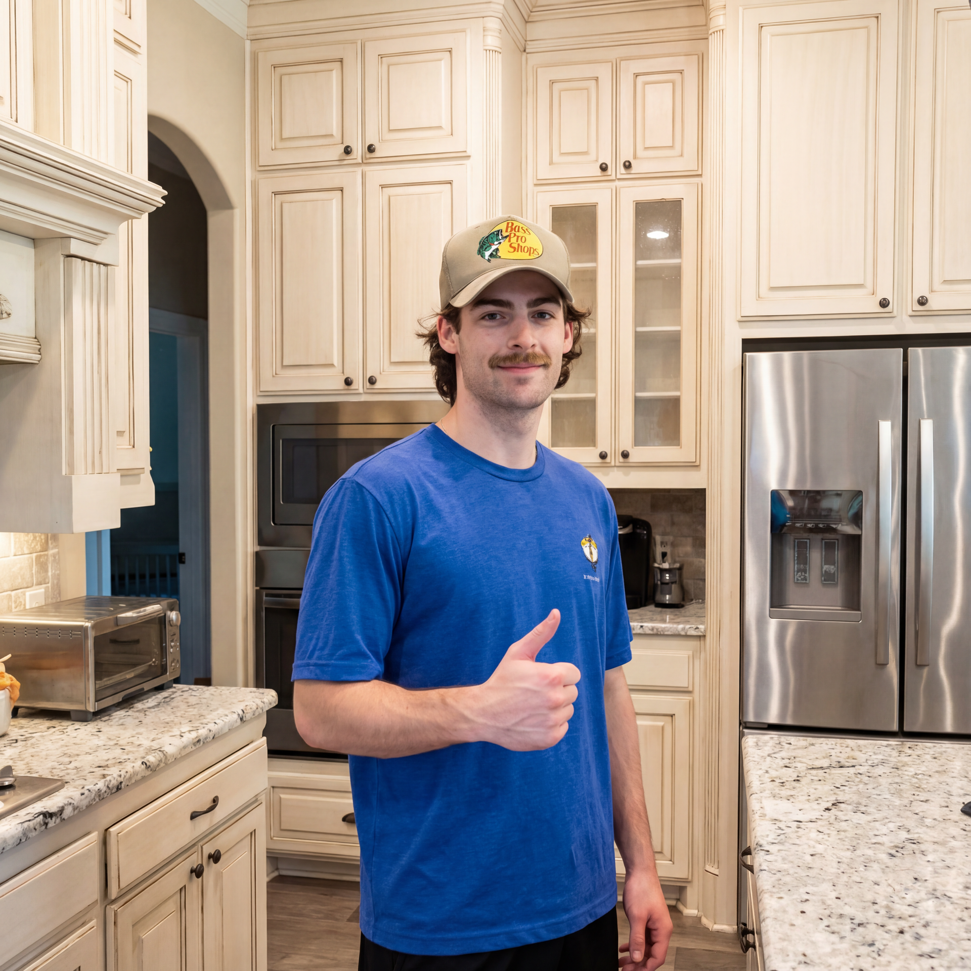 Man in a blue shirt and cap giving a thumbs-up in a bright kitchen