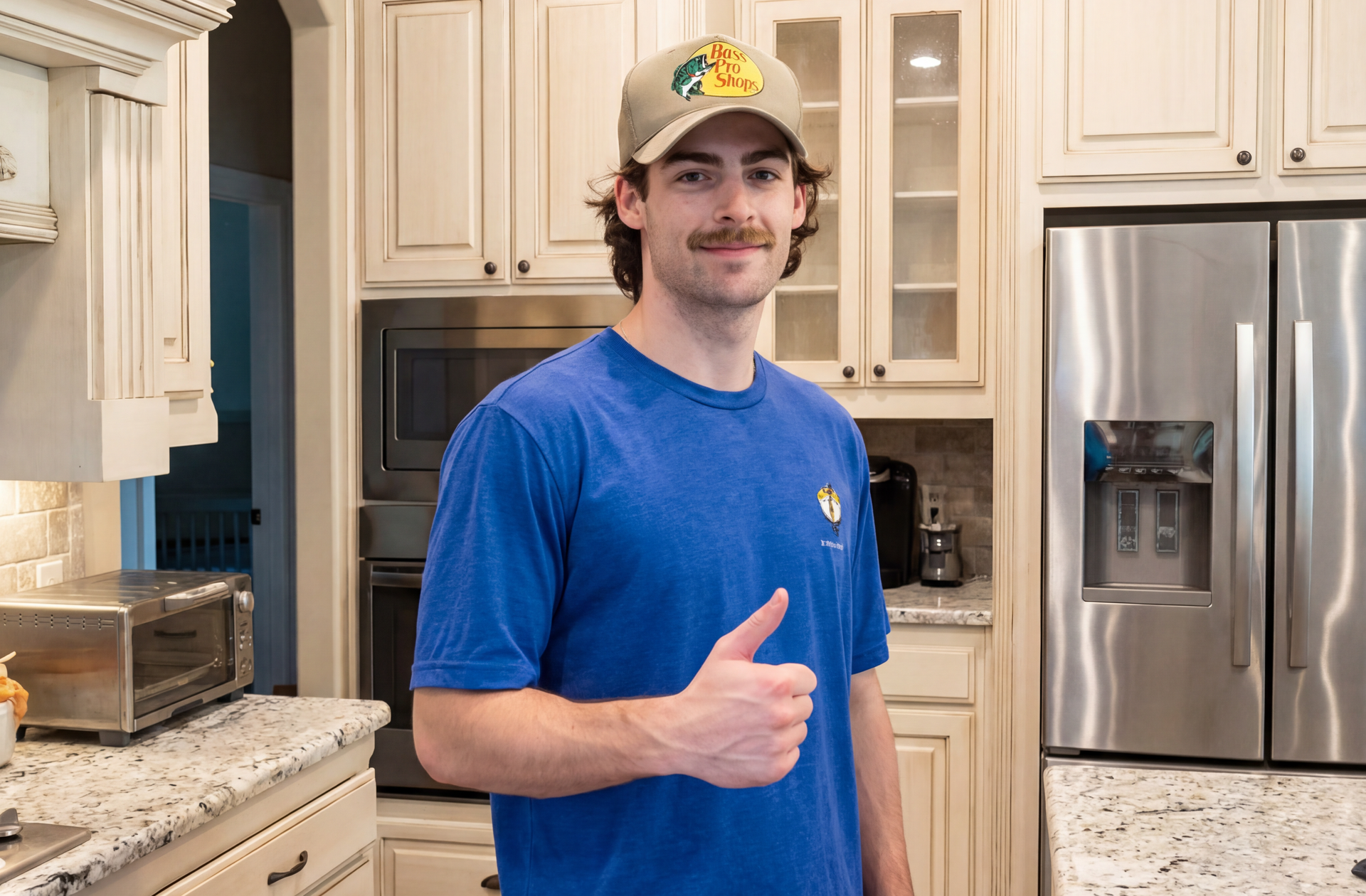 Man in blue shirt giving a thumbs-up in a bright kitchen with stainless steel appliances