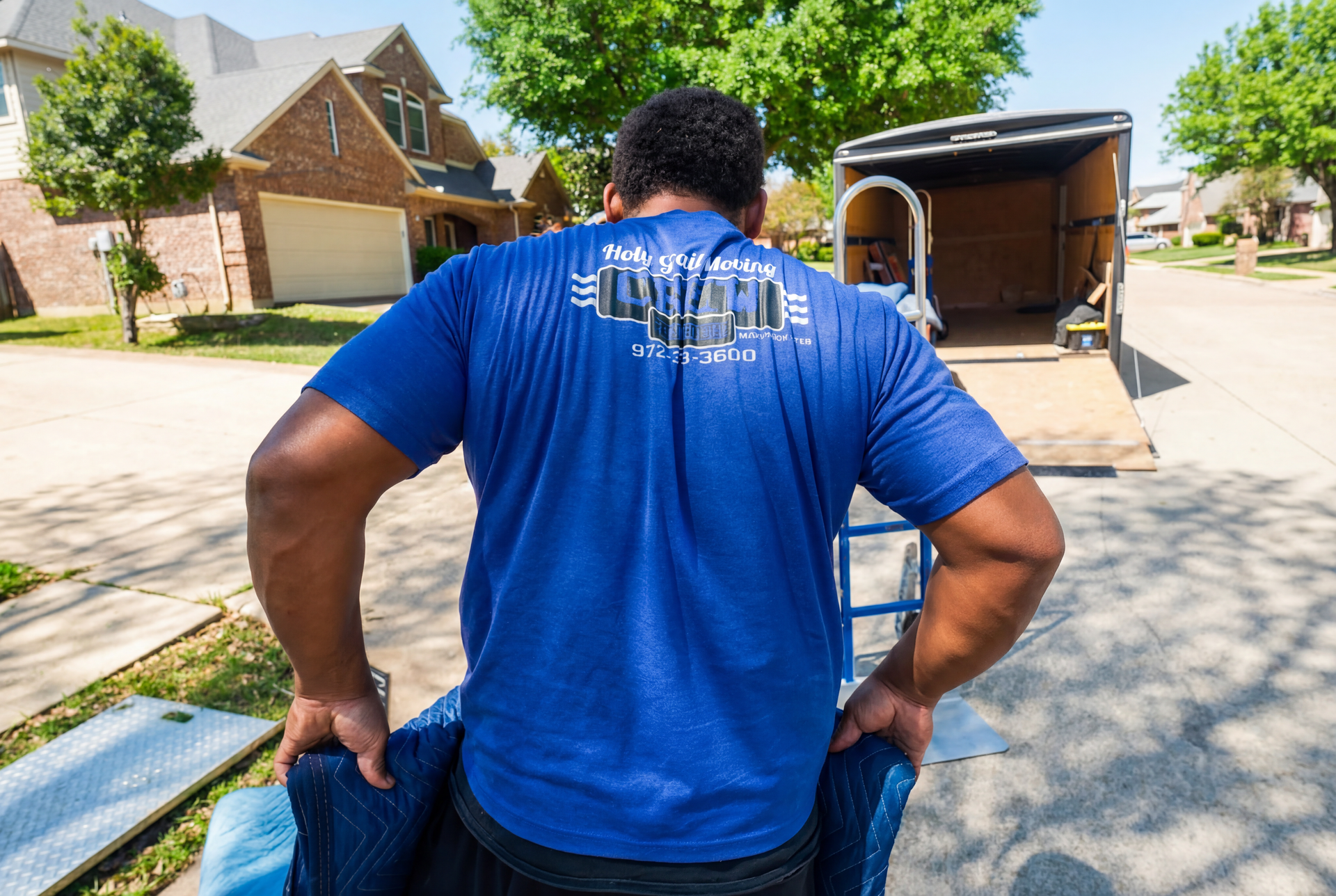 Person in a blue shirt loading items into a trailer on a suburban street.