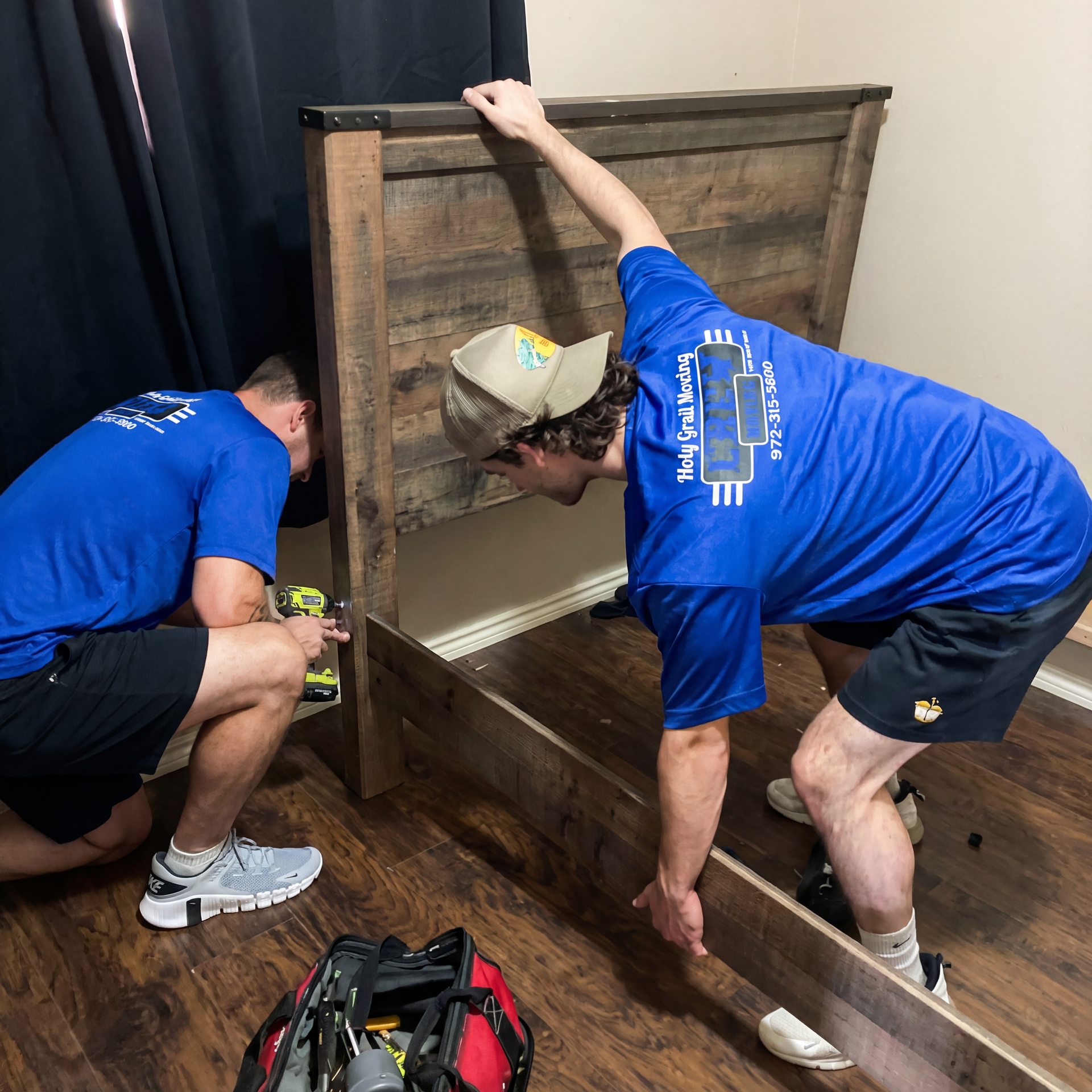 Two workers in blue shirts assembling a large wooden storage chest indoors.