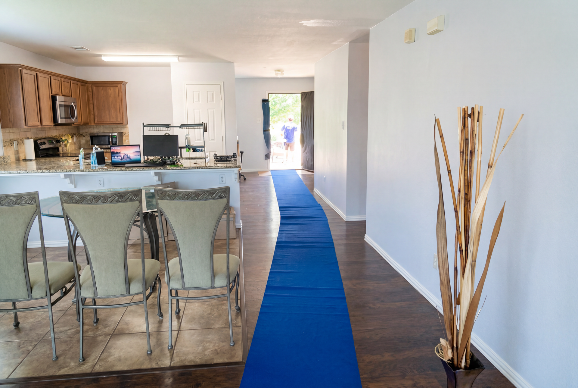 Open-plan kitchen and hallway with blue runner carpet and decorative tall sticks by the wall.