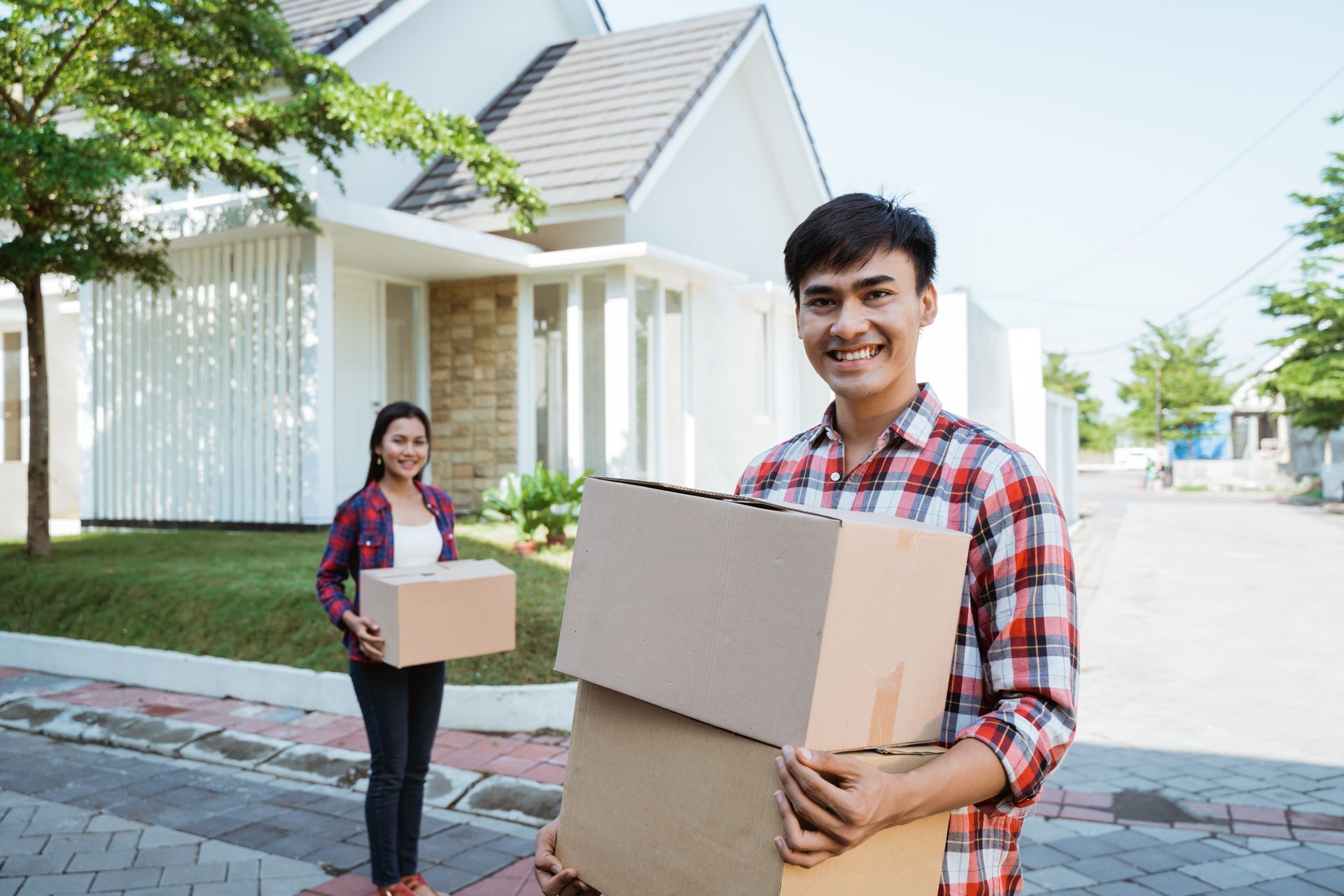 Two delivery workers carrying cardboard boxes on a sunny residential street