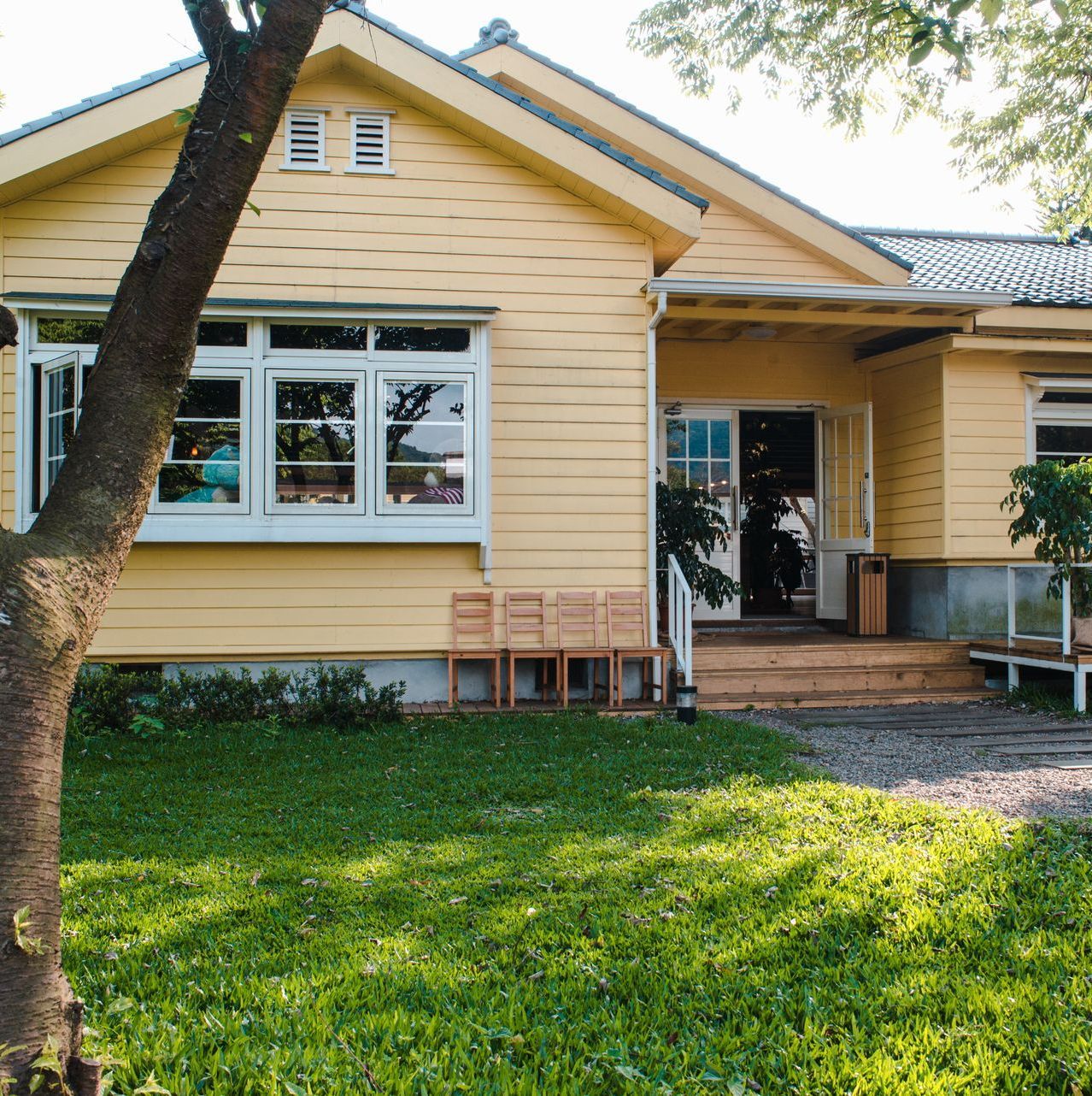 Yellow house with a front porch, large windows, and a green lawn under trees