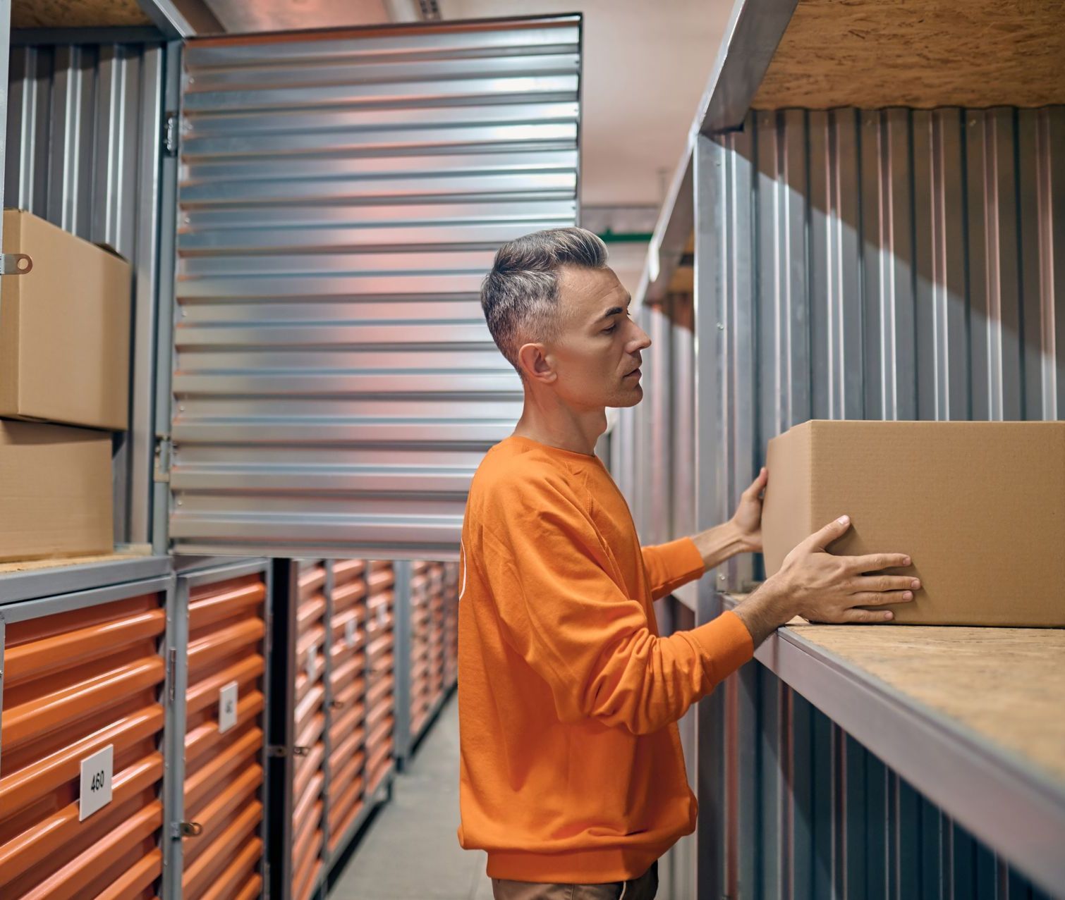 Person in orange shirt placing a box on a shelf in a storage unit.