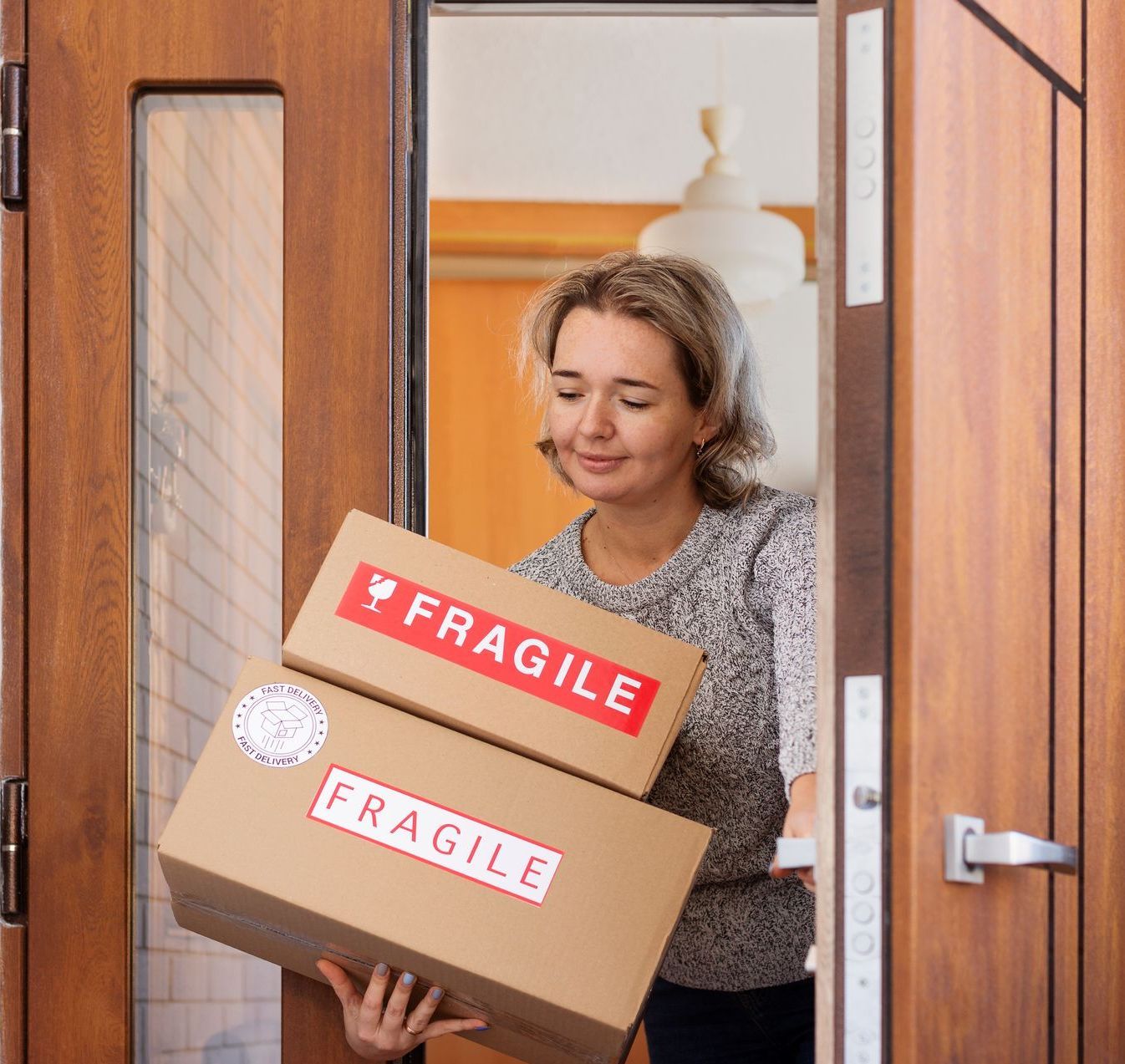 Delivery worker carrying two cardboard boxes labeled FRAGILE through a doorway