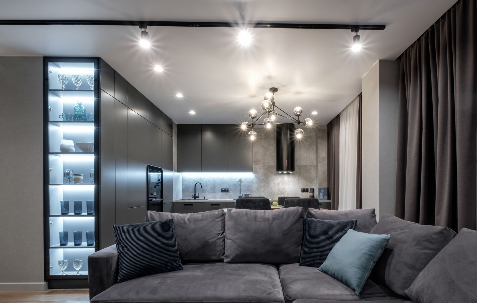 Modern gray living room with sectional sofa, pendant lights, kitchen island, and floor-to-ceiling curtains