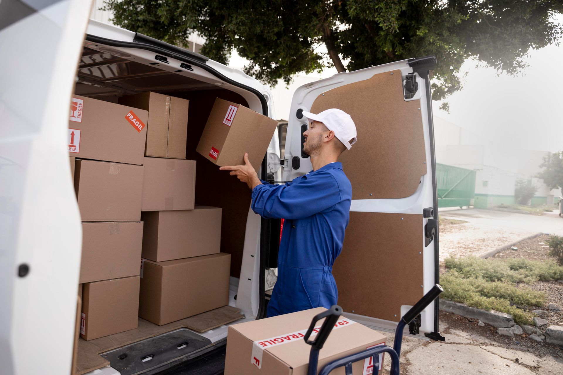 Worker in blue uniform loading cardboard boxes into a delivery van outdoors