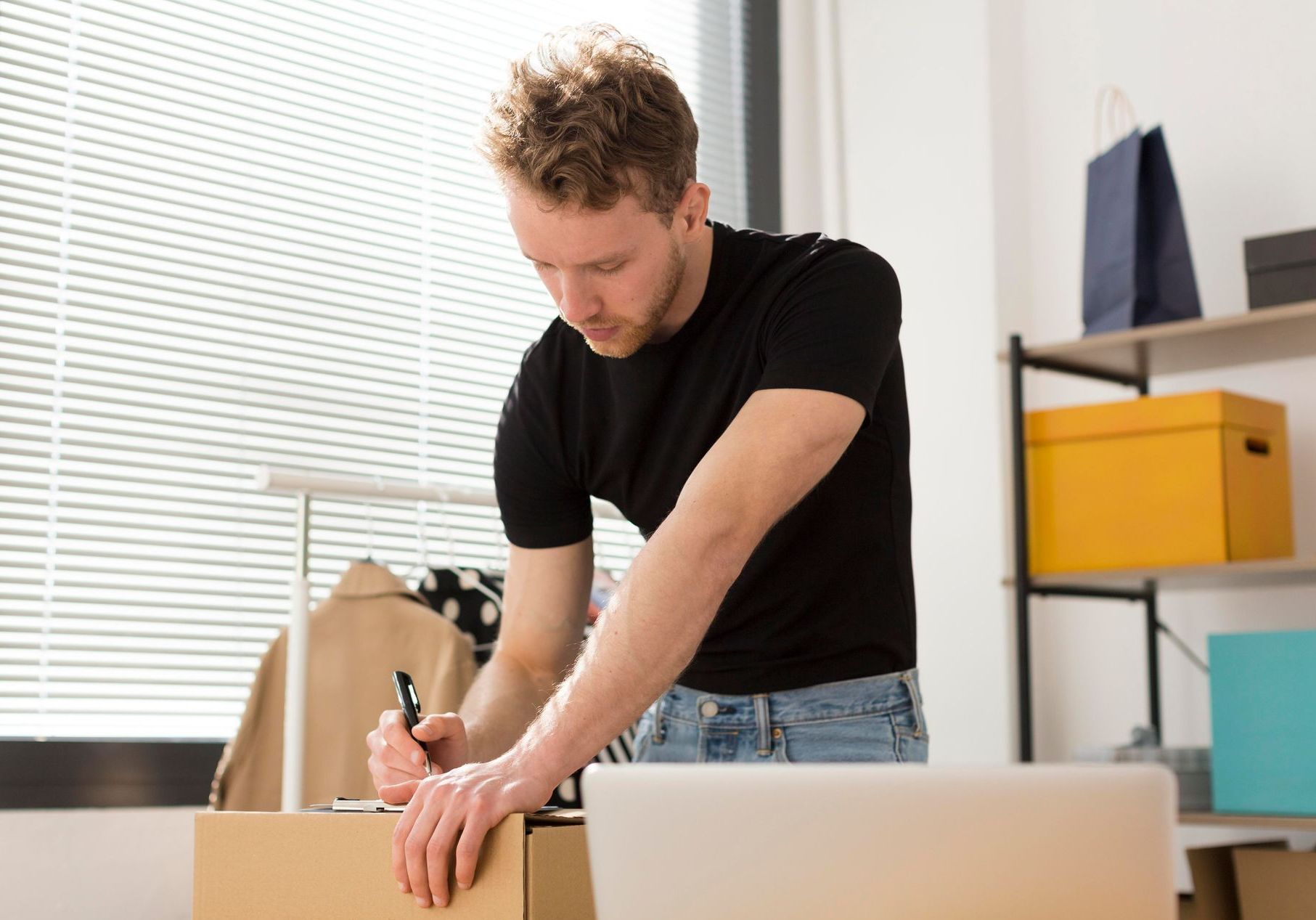 Man unpacking boxes in a bright office, opening a cardboard box on a desk